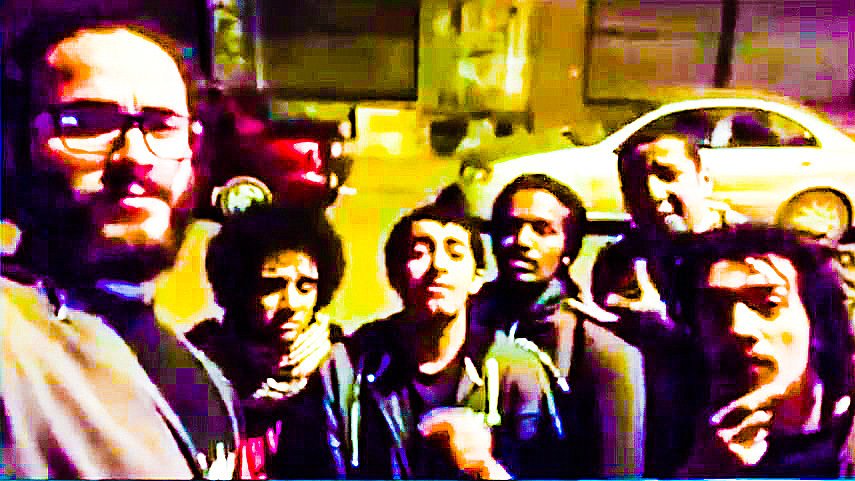 L'image montre un groupe de six personnes posant ensemble devant une voiture garée. Ils semblent être de jeunes adultes, certains portant des lunettes ou ayant des cheveux frisés. L'ambiance est détendue et amicale, et la photo semble avoir été prise de nuit, avec un éclairage un peu faible. La scène donne une impression de camaraderie et de convivialité entre les individus.