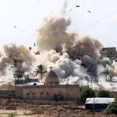 L'image montre une scène d'explosion avec de la fumée et des débris projetés dans les airs. En arrière-plan, on peut apercevoir des bâtiments, des palmiers et un terrain poussiéreux. L'explosion suggère un événement dramatique ou un conflit, et l'environnement semble rural ou semi-urbain. Des signes de destruction sont visibles, soulignant l'impact de l'explosion sur la zone environnante.