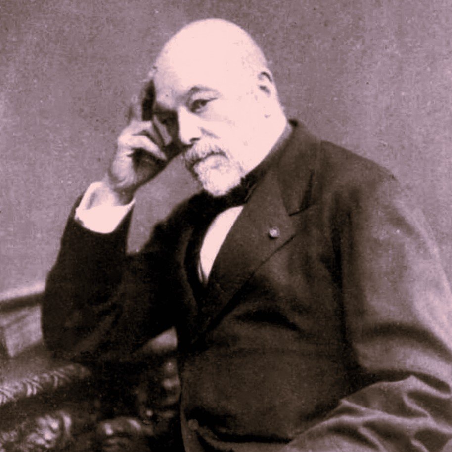 L'image montre un homme mature assis, avec une expression pensive. Il porte un costume sombre et une cravate. Sa main droite touche son menton, ce qui donne une impression de réflexion. Le fond est sombre, ce qui fait ressortir le personnage. La photographie a un style ancien, typique des portraits du 19ème siècle.