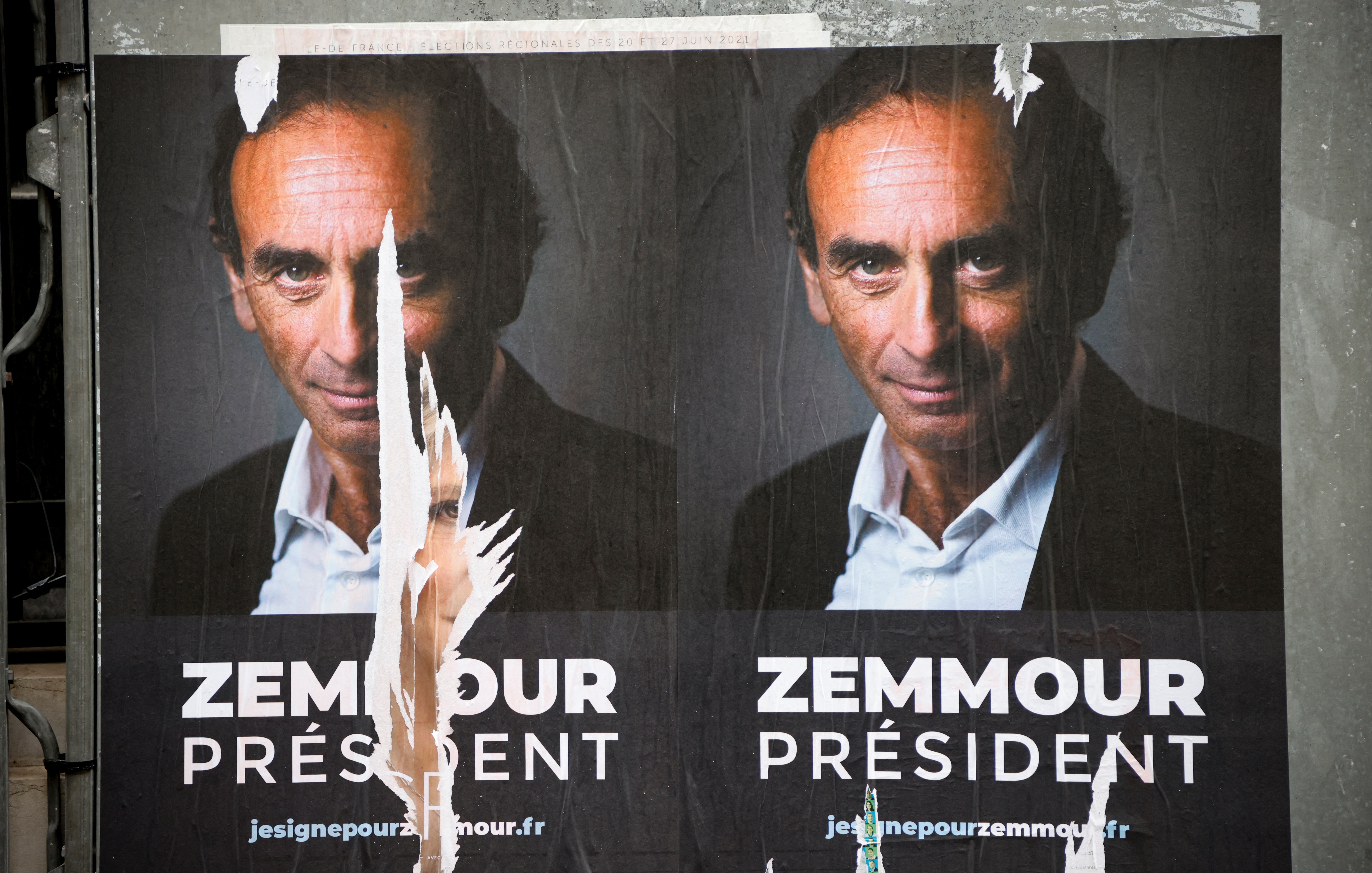 L'image montre une affiche politique présentant un homme qui se présente comme candidat à la présidence. Le visage est affiché en gros plan, et le nom "Zemmour" est écrit en grandes lettres sous le mot "PRÉSIDENT". L'affiche semble avoir été partiellement déchirée, ce qui donne un aspect usé et détérioré. On peut également remarquer un fond sombre qui met en avant le sujet de l'affiche.