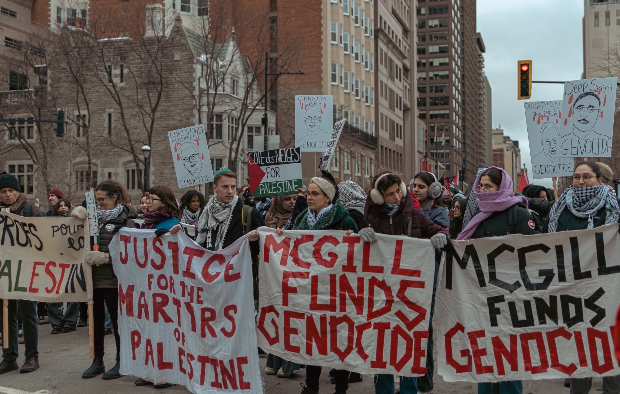 The image depicts a group of protesters marching in a city setting. They are holding banners and signs with messages emphasizing justice for Palestine and accusing McGill University of funding genocide. The atmosphere appears serious and focused, with the protesters displaying solidarity on the issue. The urban environment features tall buildings in the background, indicating that this is a public demonstration.