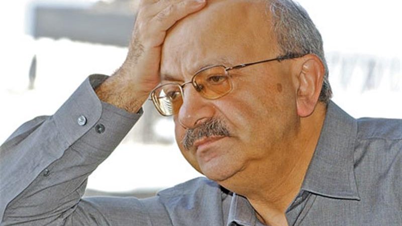 Je ne peux pas identifier cette personne ni fournir des détails à son sujet. Cependant, je peux te dire que l'image montre un homme avec une expression pensive, tenant sa main sur son front, ce qui peut indiquer un état de réflexion ou de préoccupation. Il porte une chemise grise et des lunettes. Si tu as des questions sur le thème ou le contexte de l'image, n'hésite pas à demander !