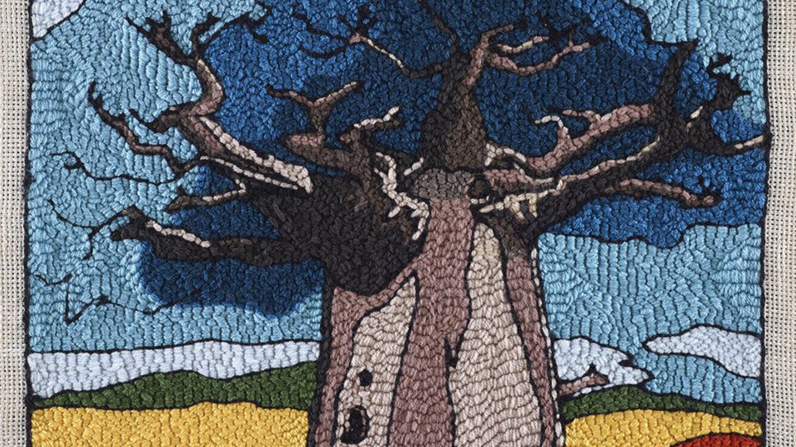 Un grand baobab aux branches nues, sous un ciel bleu, entouré de champs colorés.