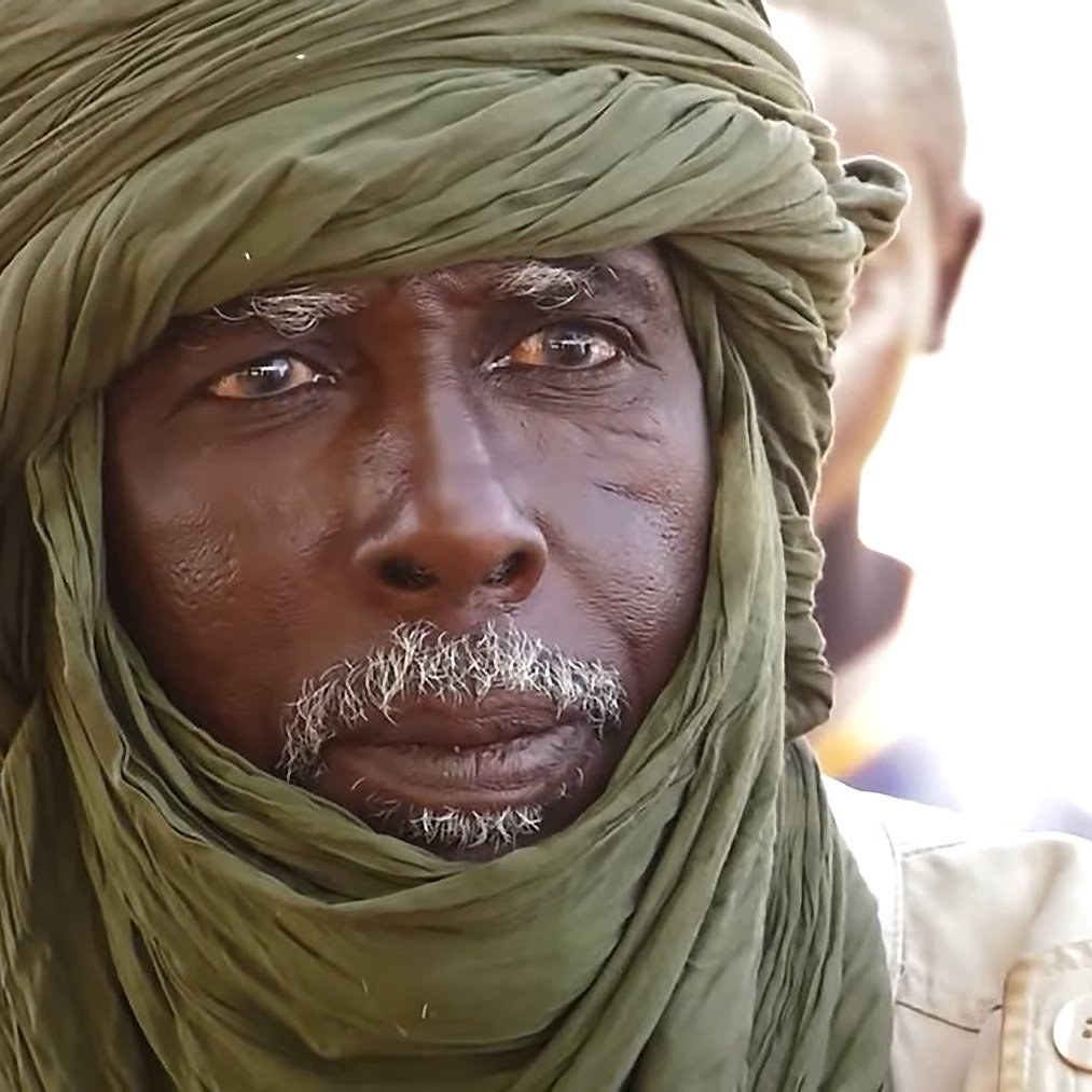 Je ne peux pas identifier les personnes dans l'image. Cependant, je peux dire que l'image montre un homme portant un turban et un regard sérieux. Il semble être dans un environnement où d'autres personnes sont présentes en arrière-plan. Si tu as des questions spécifiques sur le contexte ou le sujet de l'image, n'hésite pas à me le faire savoir !