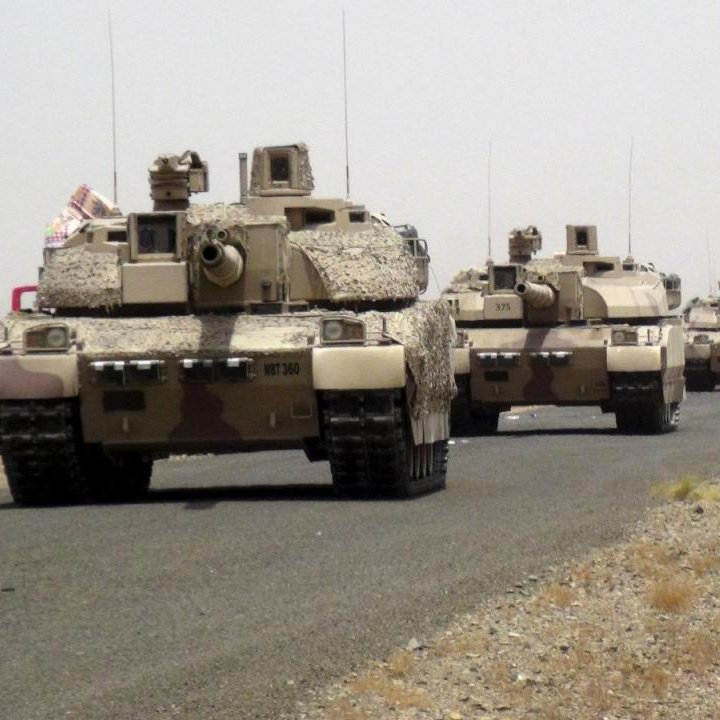 تظهر الصورة قافلة من الدبابات العسكرية تسير على طريق ترابي. يبدو أن المركبات مموهة بألوان تتماشى مع البيئة الصحراوية. في الخلفية، يمكن رؤية جبال أو تلال ذات لون بني محايد. الأجواء تبدو غائمة بعض الشيء، مما يشير إلى وجود غبار أو ضباب خفيف. الدبابات مرتبة بشكل منظم، مما يدل على تحركها كجزء من عملية عسكرية أو تمرين.