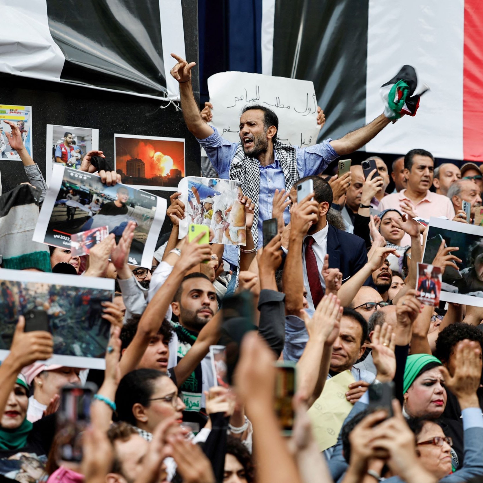 تظهر الصورة حشودًا كبيرة من الناس في تجمع أو مظاهرة. يبدو أنهم يحملون لافتات وصورًا، ويظهر في المقدمة شخص يرفع يده ويبدو أنه يتحدث إلى الجمهور. الناس في الخلف يحملون أعلامًا وصورًا، ما يدل على أنهم يعبرون عن مشاعر قوية، ربما تتعلق بقضية سياسية أو اجتماعية. يبدو أن الجو مليء بالحماس والتفاعل.