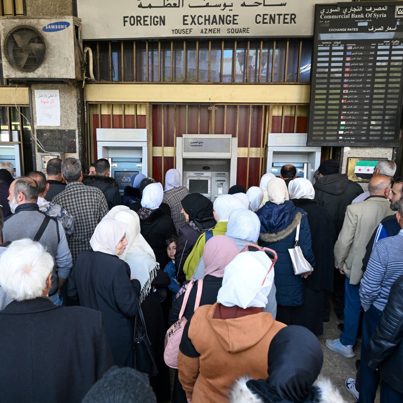 Une foule de personnes fait la queue devant un guichet bancaire.