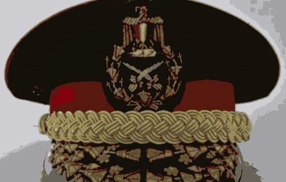 L'image montre un uniforme militaire, plus précisément un couvre-chef. Il s'agit d'une casquette ou d'un képi avec une visière. Le chapeau est décoré de divers ornements en métal ou en broderie, incluant un insigne central représentant des attributs militaires. On peut observer également une bordure en or ou en couleur claire qui donne une impression de prestige. Les détails suggèrent que ce couvre-chef est associé à un grade élevé dans une force armée.
