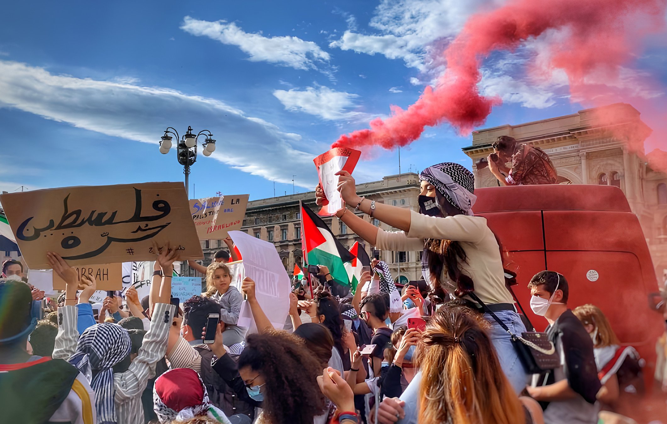 Una manifestazione colorata con fumogeni rossi e cartelli per la Palestina.
