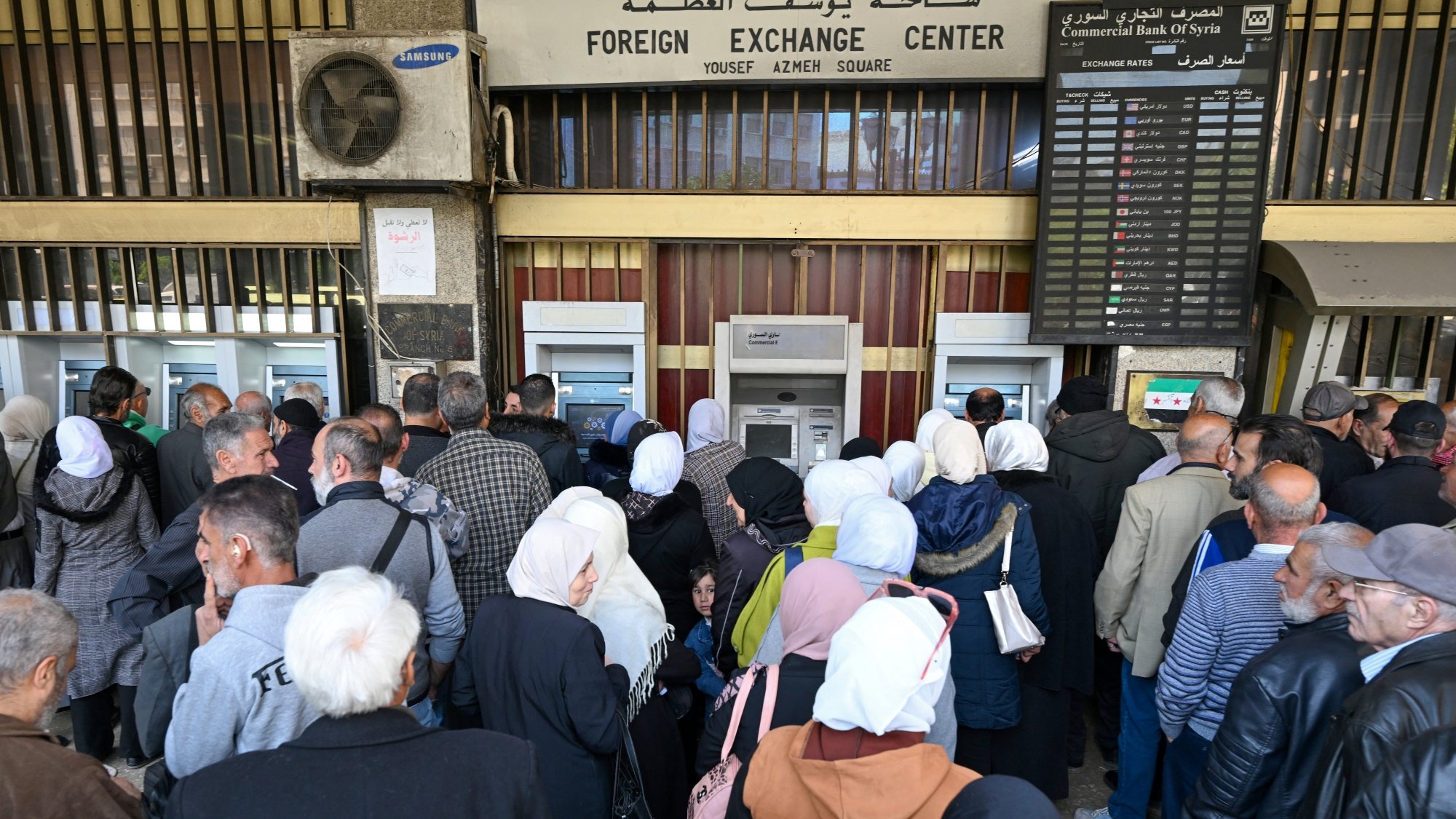 Une foule de personnes fait la queue devant un guichet bancaire.