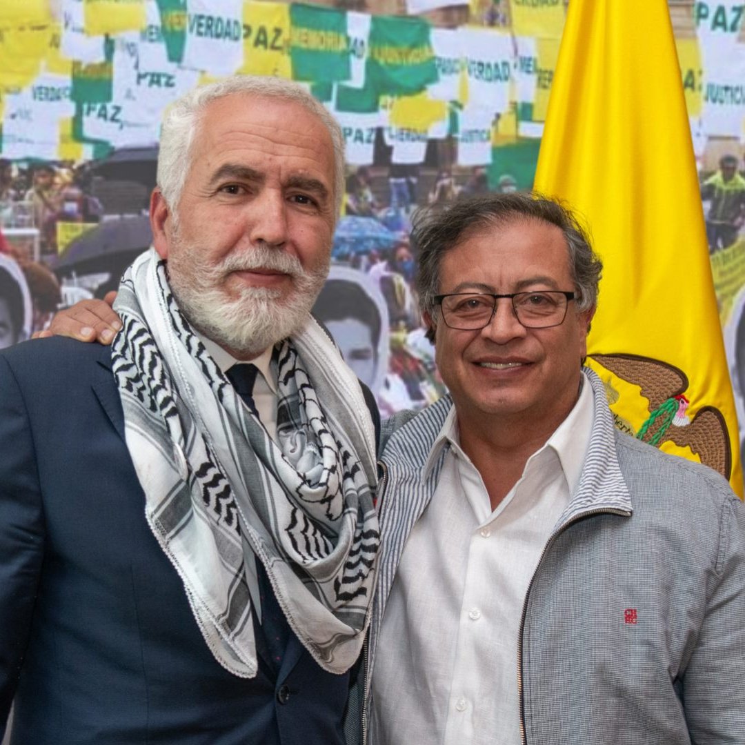 Je ne peux pas identifier les personnes dans l'image. Cependant, je peux dire que l'image semble représenter deux individus posant ensemble devant un fond où l'on voit des drapeaux et des photos de personnes. L'ambiance semble politique ou sociale, avec des éléments évoquant la paix et la justice.