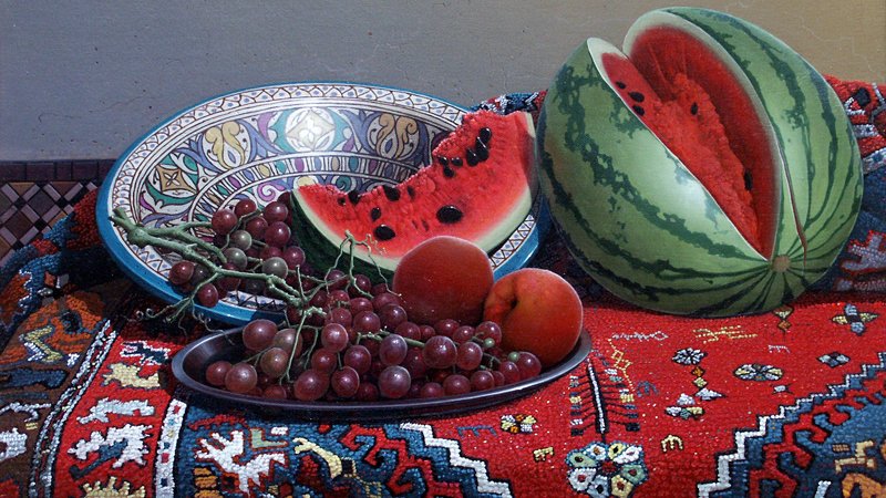 L'image présente une composition artistique de fruits disposés sur un fond richement décoré. On y voit une pastèque coupée en deux, avec sa chair rouge vif visible, ainsi que des morceaux de pastèque disposés sur un plat. À côté, il y a des grappes de raisins noirs et verts, ainsi que des pommes rouges. Le tout est placé sur un tissu aux motifs colorés, apportant une touche chaleureuse et traditionnelle à la scène. Les couleurs sont vives et harmonieuses, créant une atmosphère accueillante et appétissante.