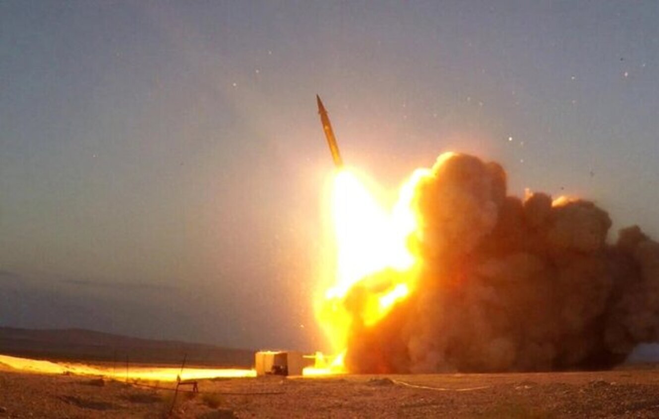 تصویر نشان‌دهنده‌ی پرتاب یک موشک است. در این صحنه، لحظه‌ای از پرتاب موشک به تصویر کشیده شده که شعله‌های آتش و دود فراوانی به سمت آسمان منتشر می‌شود. موشک به طور عمودی از یک سکوی پرتاب خارج شده و محیط اطراف آن نیز کاملاً روشن شده است. نور ناشی از آتش و انفجار به وضوح در تصویر قابل مشاهده است و زمینه نیز به وضوح نشان‌دهنده‌ی زمین خشک و بیابانی است.