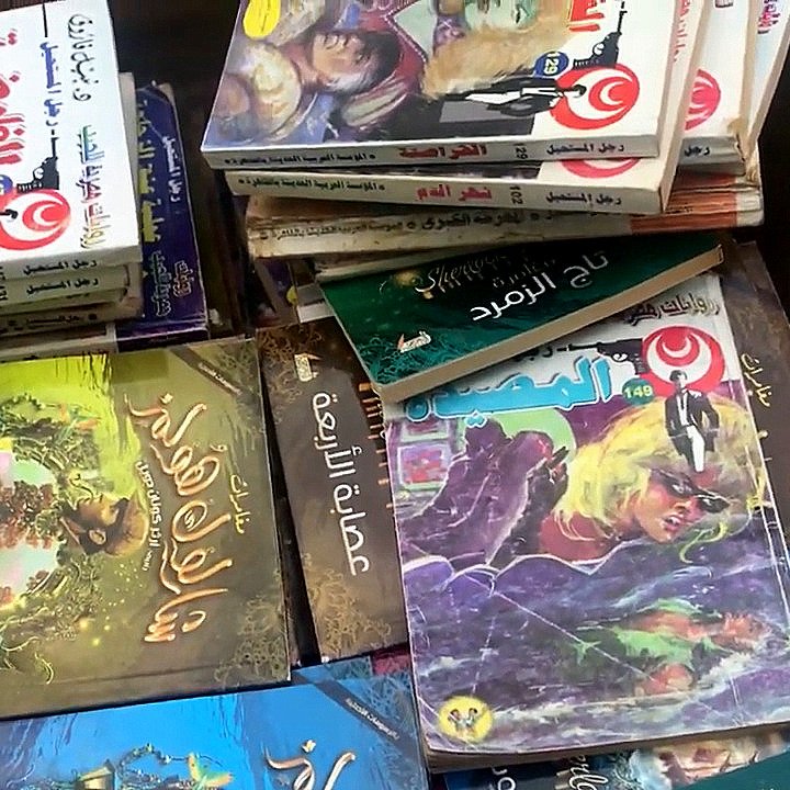 L'image montre une boîte remplie de livres empilés les uns sur les autres. On peut apercevoir différents titres en arabe sur les couvertures, illustrés par des images colorées. Certains livres semblent appartenir à des séries de contes ou de romans graphiques, avec des illustrations captivantes et des textes en arabe. L'ensemble donne une impression d'abondance littéraire.