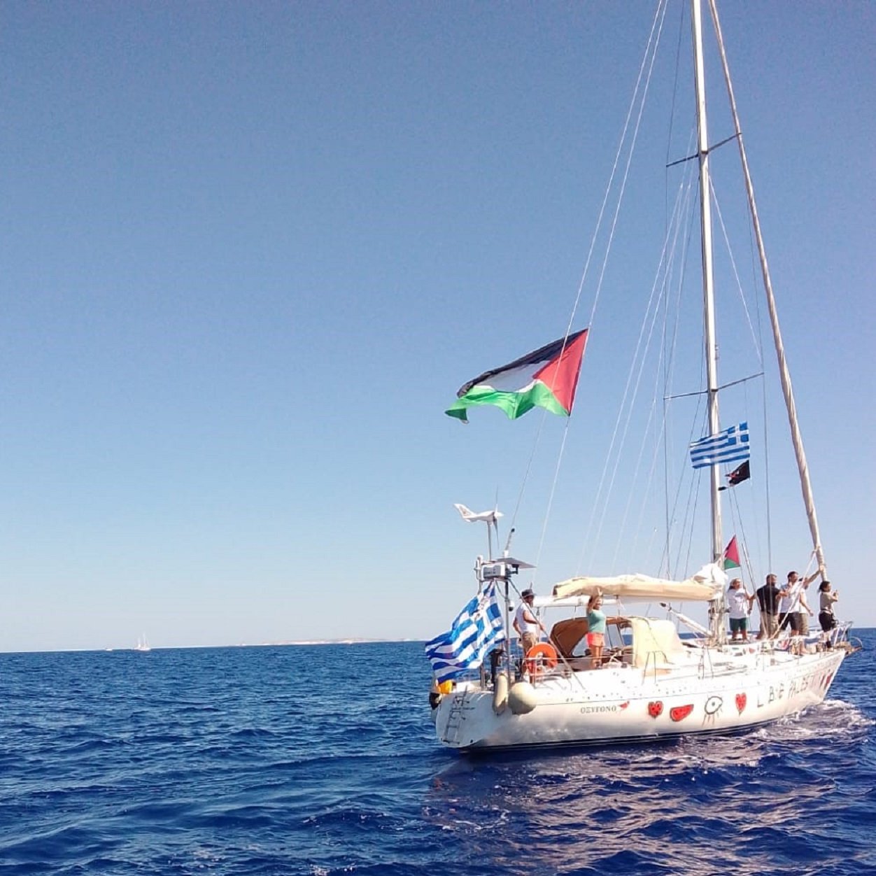 Un voilier sur la mer, arborant plusieurs drapeaux, sous un ciel bleu.