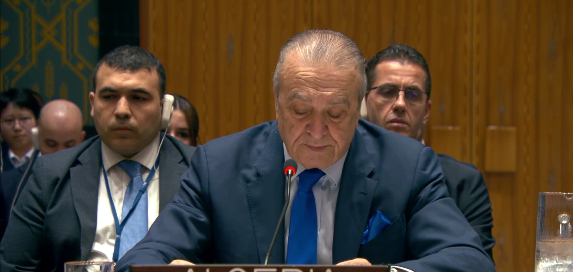 A man in a suit speaks at a podium labeled "Algeria" in a formal setting with delegates behind him.