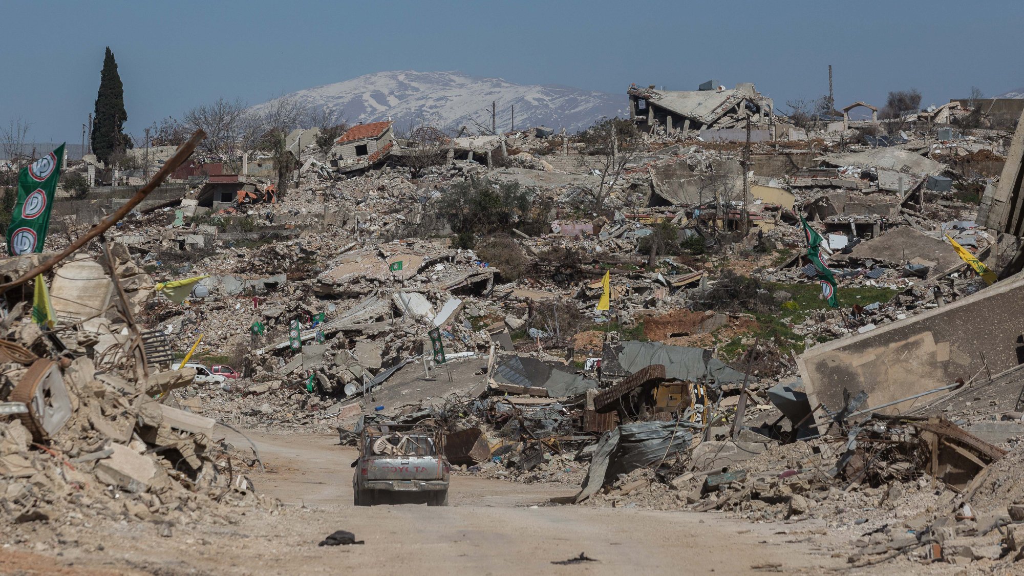 Un paysage dévasté avec des bâtiments en ruines et des montagnes enneigées au loin.