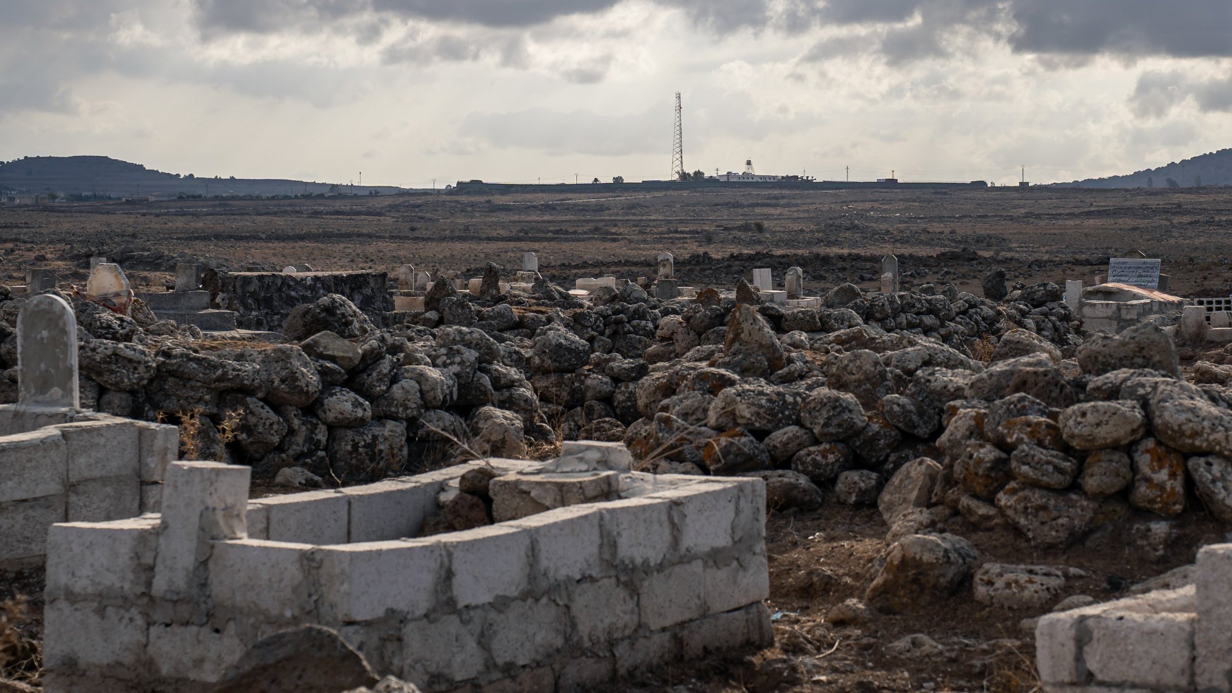 Un paysage aride avec des tombes et des pierres, sous un ciel nuageux.