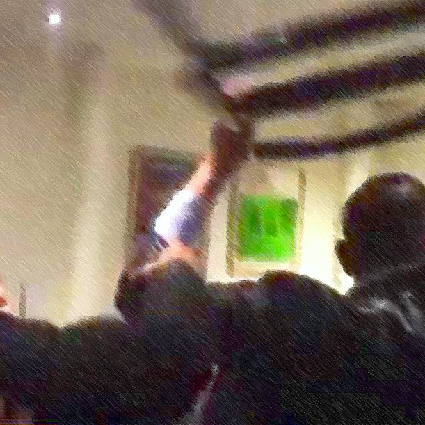 L'image montre un groupe de personnes se rassemblant autour d'une bannière ou d'un drapeau, qu'ils soulèvent. L'atmosphère semble dynamique et engagée, avec des individus exprimant leurs émotions. Le fond est flou, ce qui met l'accent sur l'action au premier plan. On peut sentir une ambiance de solidarité ou de protestation.