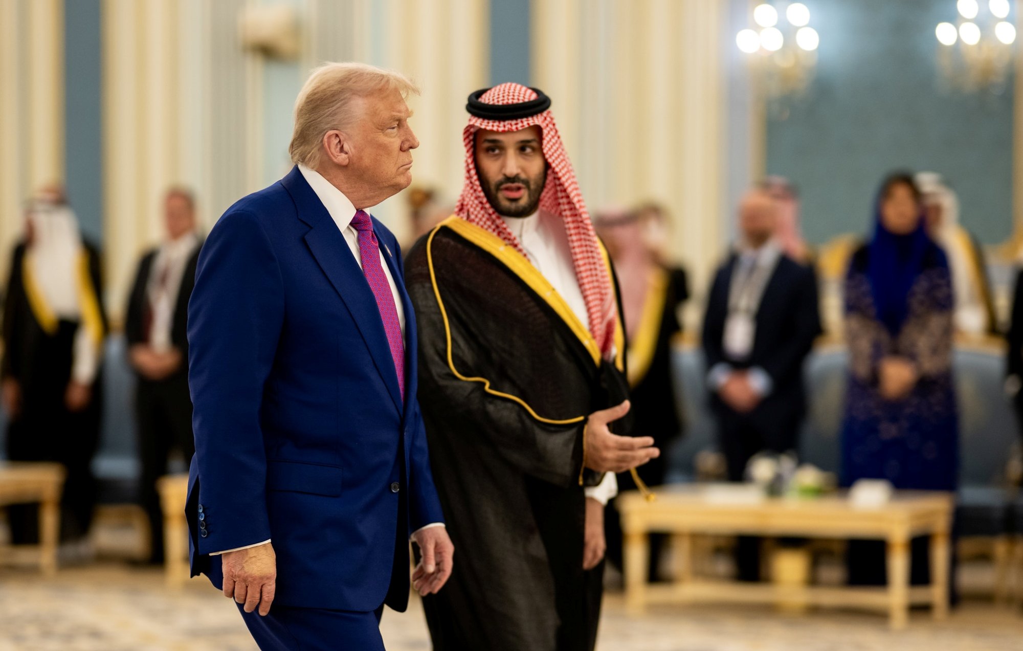 Deux hommes en costume, l'un américain et l'autre saoudien, discutent dans un hall élégant.