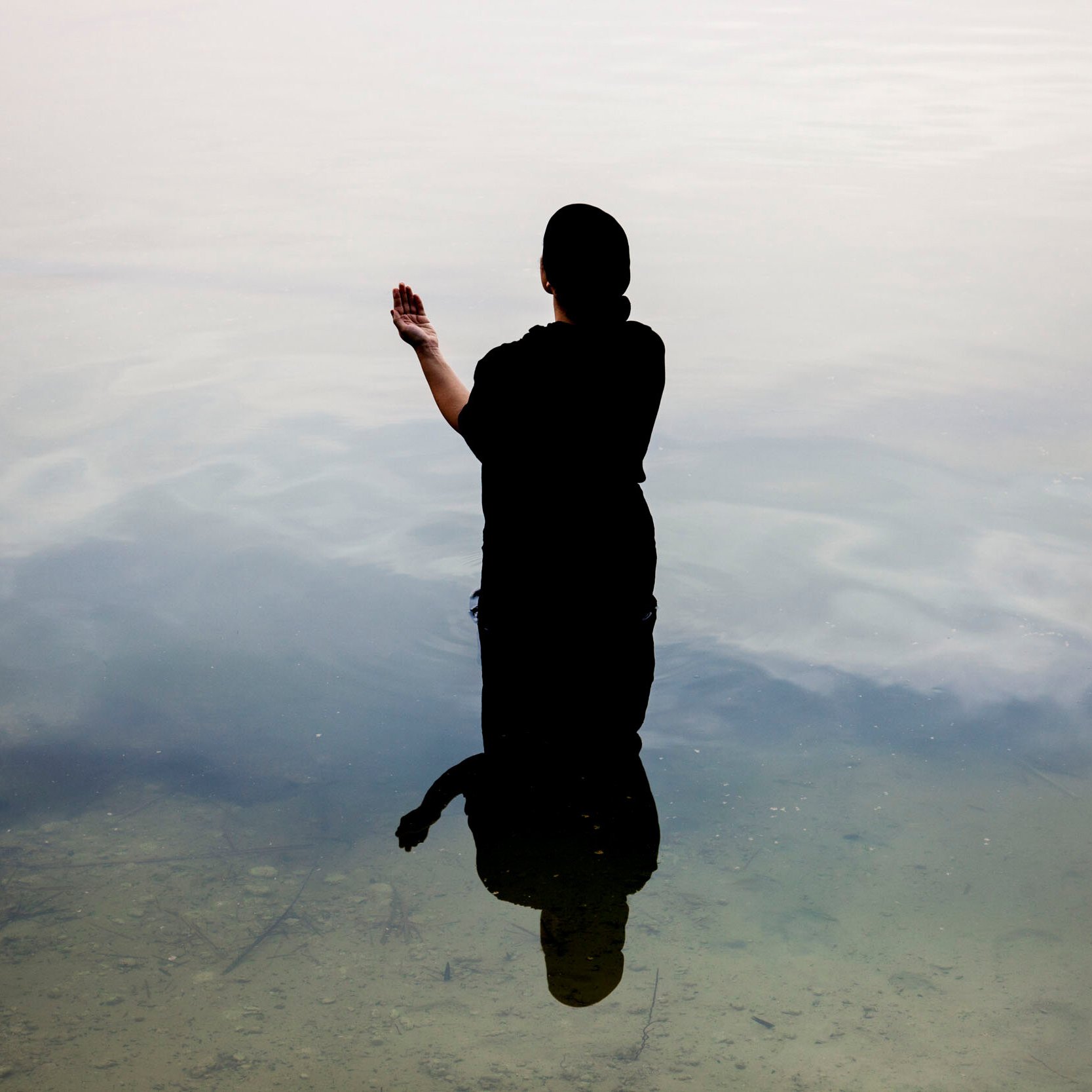 Une silhouette noire se tient dans l'eau calme, reflet visible à la surface.