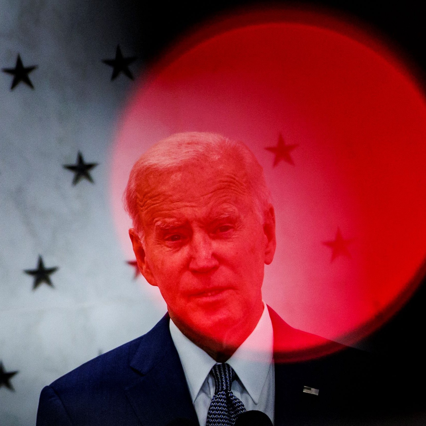 L'image montre un homme en train de parler, probablement lors d'un discours. En arrière-plan, on peut voir un motif de petites étoiles qui s'étale sur une surface claire. Une lumière rouge qui semble provenir de l'avant-plan crée un flou, accentuant la figure de l'homme et lui donnant une apparence distincte. L'atmosphère de l'image semble sérieuse ou solennelle, suggérant un événement important.