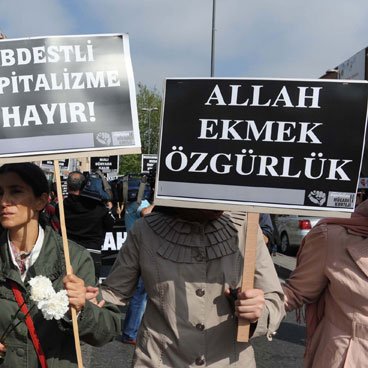 L'image montre une manifestation avec des personnes portant des pancartes. Les manifestants semblent exprimer des revendications contre la pression et l'oppression, en mettant en avant des messages en turc. Certaines femmes portent des foulards, suggérant un contexte culturel spécifique. On peut sentir une atmosphère de mobilisation collective.