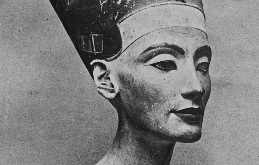 L'image montre un buste sculpté d'une femme portant une couronne élevée et un collier élaboré. Ce buste est souvent associé à la célèbre reine égyptienne Néfertiti. Les traits du visage sont raffinés et symétriques, avec des yeux en amande et des lèvres délicates. La couronne est ornée de motifs distinctifs, et le collier est décoré de détails géométriques. L'œuvre fait partie de l'art égyptien ancien, symbolisant la beauté et l'élégance de l'époque.