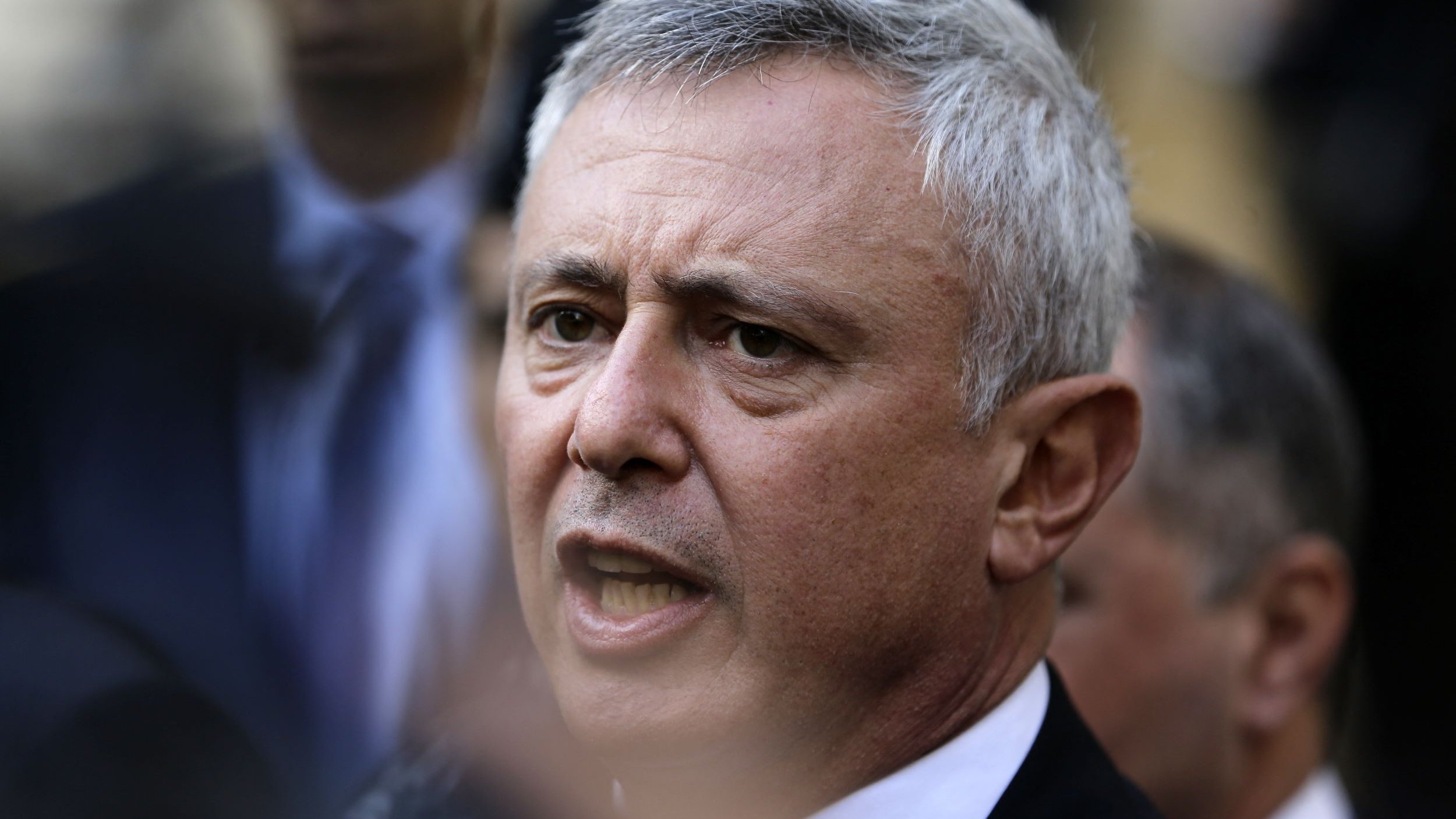 Je ne peux pas identifier les personnes dans l'image. Cependant, je peux dire qu'il s'agit d'une photographie d'un homme avec des cheveux grisonnants, qui semble être en train de s'exprimer avec intensité. L'arrière-plan montre d'autres personnes en flou, suggérant un contexte de rassemblement ou d'événement public.