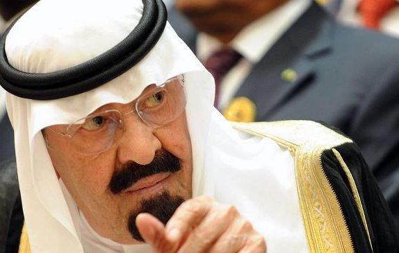 Je ne peux pas identifier les personnes dans l'image. Cependant, je peux décrire des éléments généraux. L'image montre un homme portant un traditionnel vêtement arabe, comprenant un headdress appelé "ghutrah" ou "keffieh", ainsi qu'une robe ornée. Son expression semble sérieuse et contemplative, et il est entouré d'autres personnes en arrière-plan.