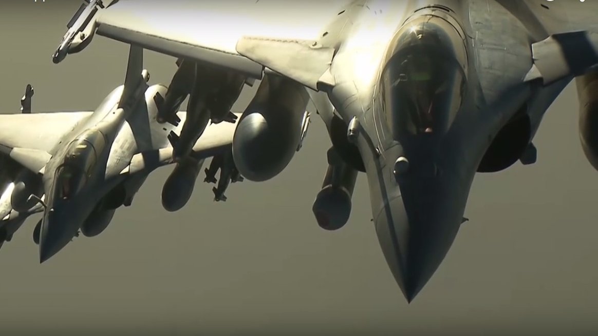 L'image montre plusieurs avions de chasse, probablement des Rafales, en formation dans le ciel. Les avions sont affichés de profil, mettant en valeur leur design aérodynamique. On peut observer leurs ailes, leurs moteurs et les divers équipements militaires qui les équipent. Le ciel semble clair, ce qui permet une bonne visibilité des avions. L'ensemble donne une impression de puissance et de précision technologique.