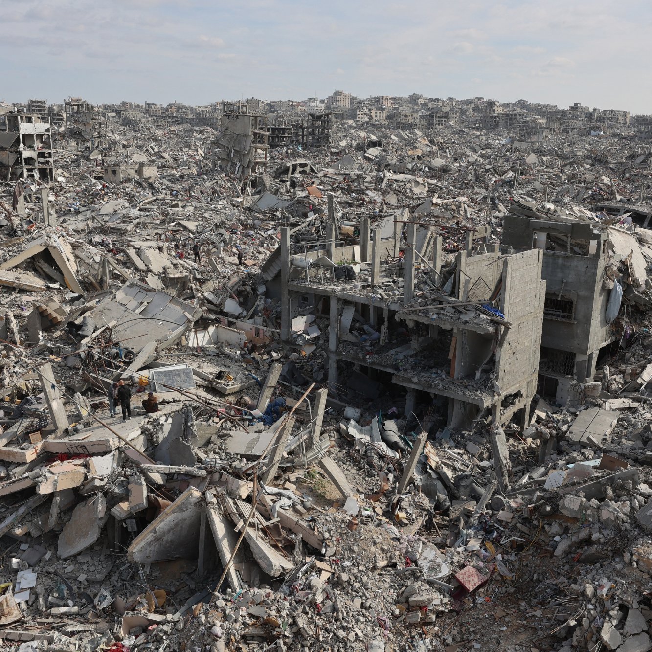 L'immagine mostra un vasto paesaggio di distruzione, con edifici in rovina e detriti sparsi ovunque. Ci sono strutture crollate e macerie che si estendono fino all'orizzonte, creando un'atmosfera di desolazione e abbandono.