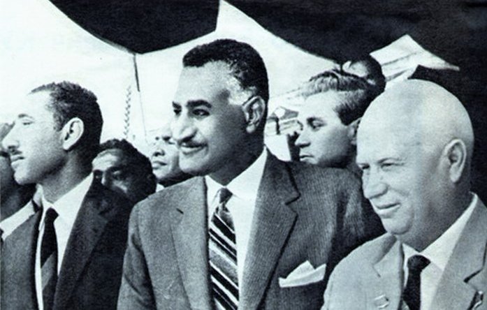 الصورة تظهر ثلاثة رجال يقفون في حدث رسمي. الرجل في المنتصف يرتدي بدلة أنيقة مع ربطة عنق، ويظهر عليه مظهرٌ واثق. الشخصان الآخران على جانبيه يبدو أنهم يرتدون ملابس رسمية أيضًا. يبدو أن البيئة من حولهم تشير إلى مناسبة مهمة. للحظة، يبدو أنهم يتحدثون أو يتبادلون الآراء حول موضوع ما. الصورة تحمل طابعًا تاريخيًا، ربما تشير إلى فترة معينة في السياسة أو العلاقات الدولية.