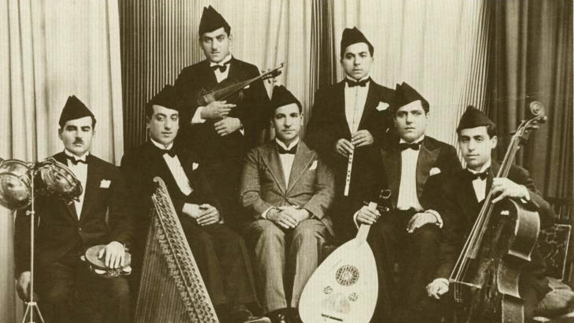Groupe de musiciens en costume noir, instruments variés, ambiance d'époque.