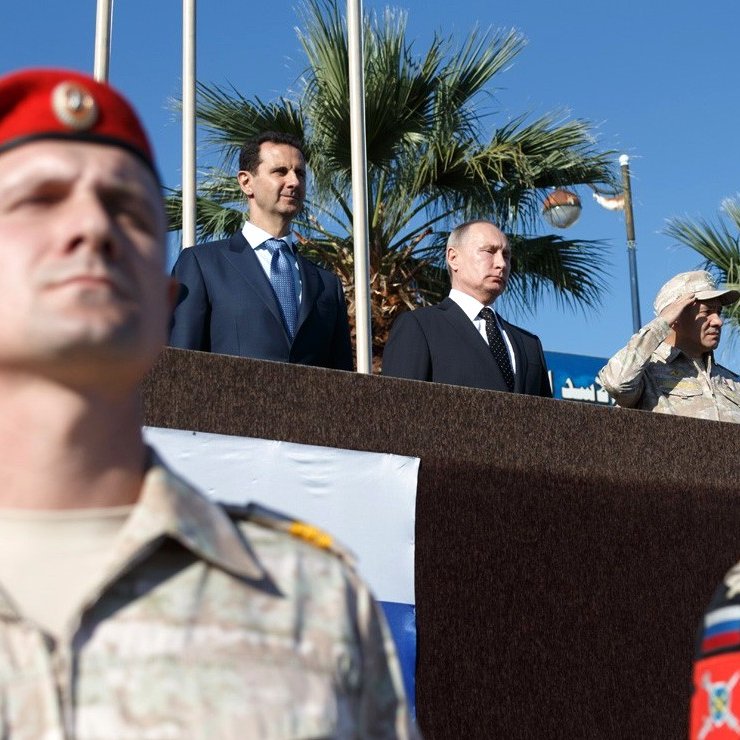 در این تصویر، گروهی از نظامیان در جلوی سن قرار دارند و به نظر می‌رسد که برگزارکننده یک مراسم رسمی هستند. دو نفر در بالای سن ایستاده‌اند؛ یکی از آن‌ها در لباس رسمی و دیگری در لباس نظامی است. پرچم‌های مختلفی در تصویر وجود دارد که نشان‌دهنده کشورهای مختلف هستند. محیط به طور کلی به نظر می‌رسد که در یک فضای باز و شاید در کنار دریا باشد، زیرا درختان نخل در پس‌زمینه دیده می‌شوند. نور خورشید به خوبی در تصویر منعکس شده و جو مراسم رسمی و شکوهمندی را به تصویر می‌کشد.