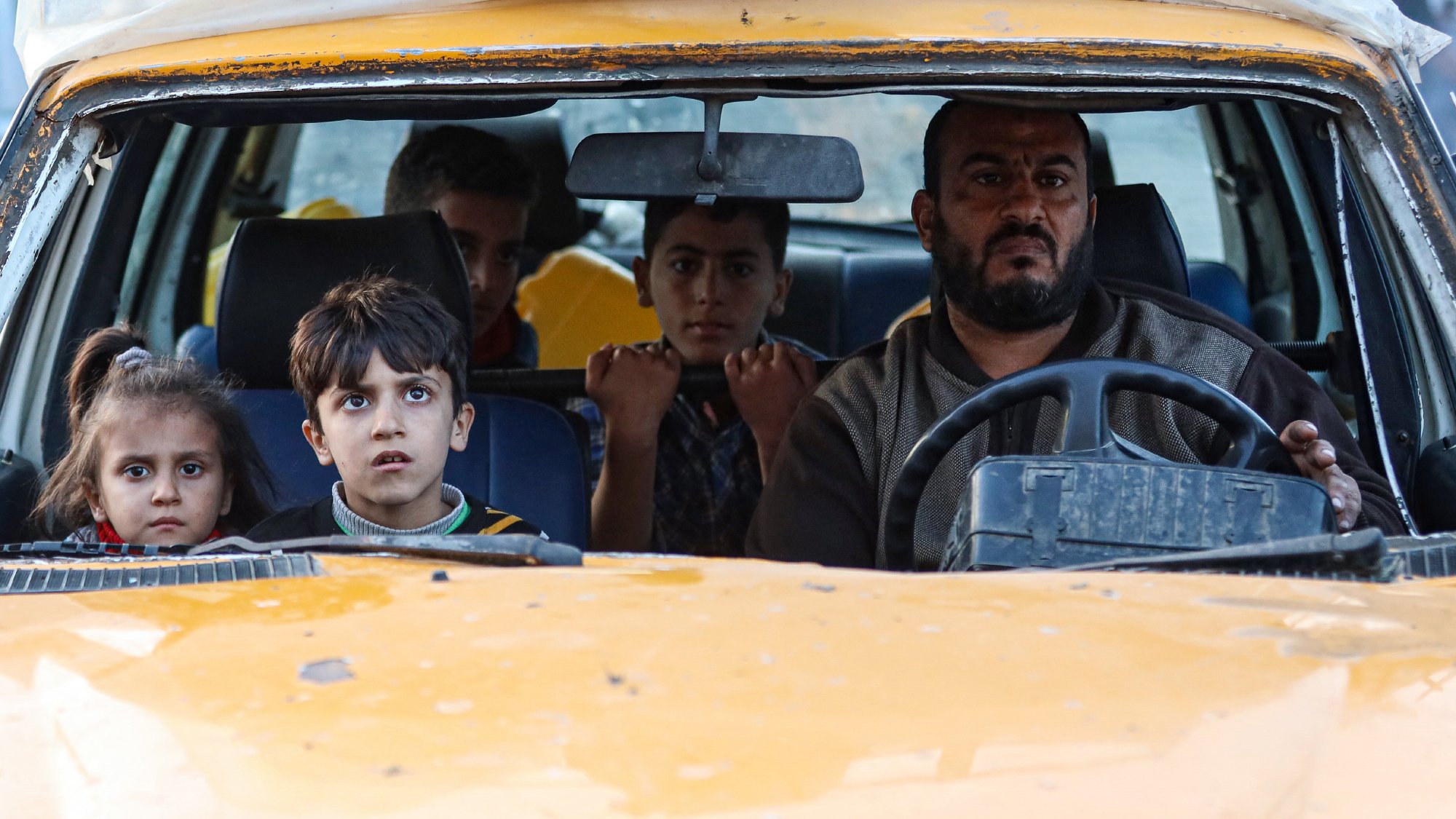 Un uomo alla guida di un'auto con bambini nel sedile anteriore, sguardi preoccupati.