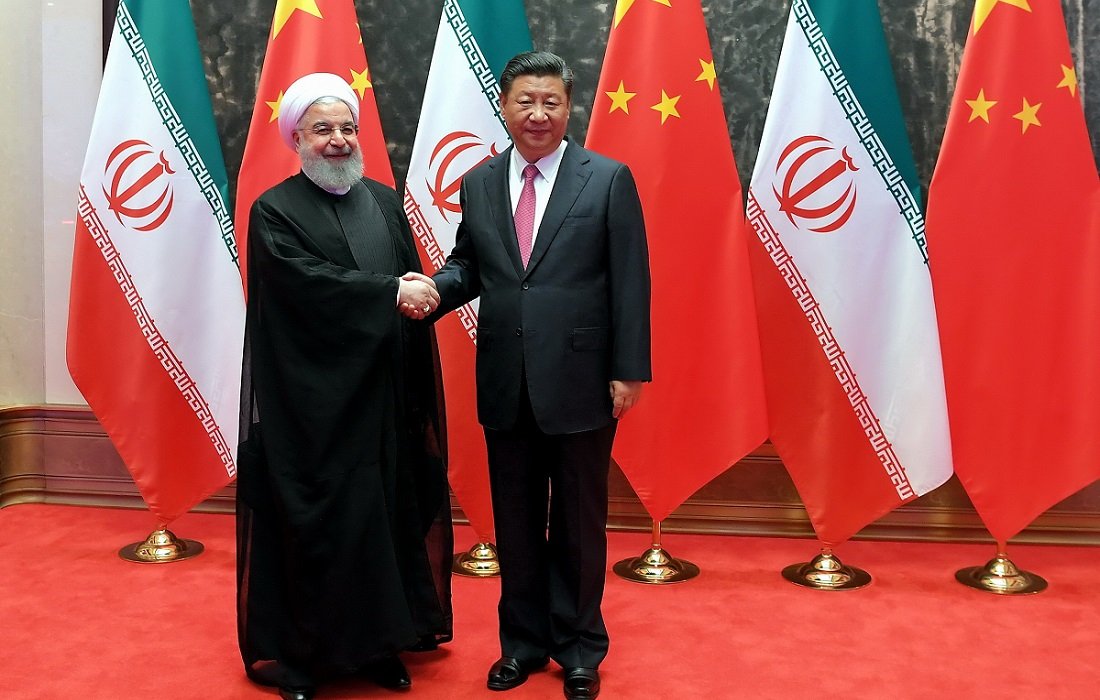 L'image montre deux dirigeants se serrant la main, souriant, devant un fond composé de drapeaux. À gauche, une figure en habit traditionnel noir, probablement d'origine iranienne, et à droite, un homme en costume sombre avec une cravate rouge, représentant probablement la Chine. Le décor inclut des drapeaux chinois et iraniens, soulignant une rencontre diplomatique entre les deux pays. Le tapis rouge au sol ajoute une touche officielle à l'événement.