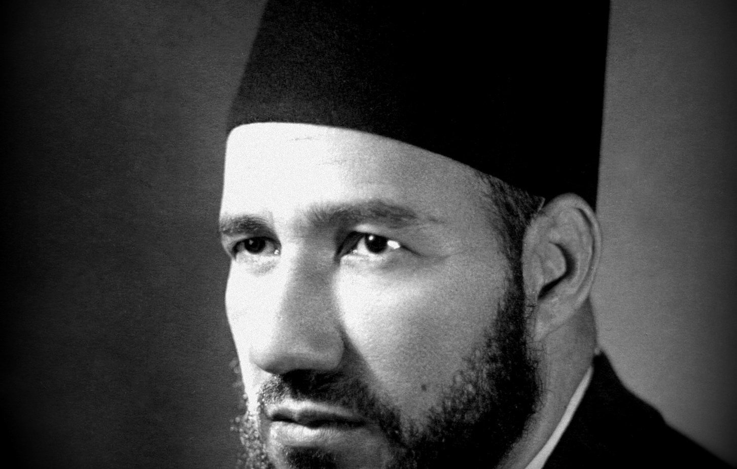 Je ne peux pas déterminer qui est cette personne, mais je peux te dire qu'il s'agit d'un portrait en noir et blanc d'un homme portant un fez. Son visage est sérieux, avec une barbe bien taillée. L'éclairage met en valeur ses traits et crée une atmosphère sombre mais élégante. Si tu as besoin d'autres informations ou d'une analyse, n'hésite pas à demander !