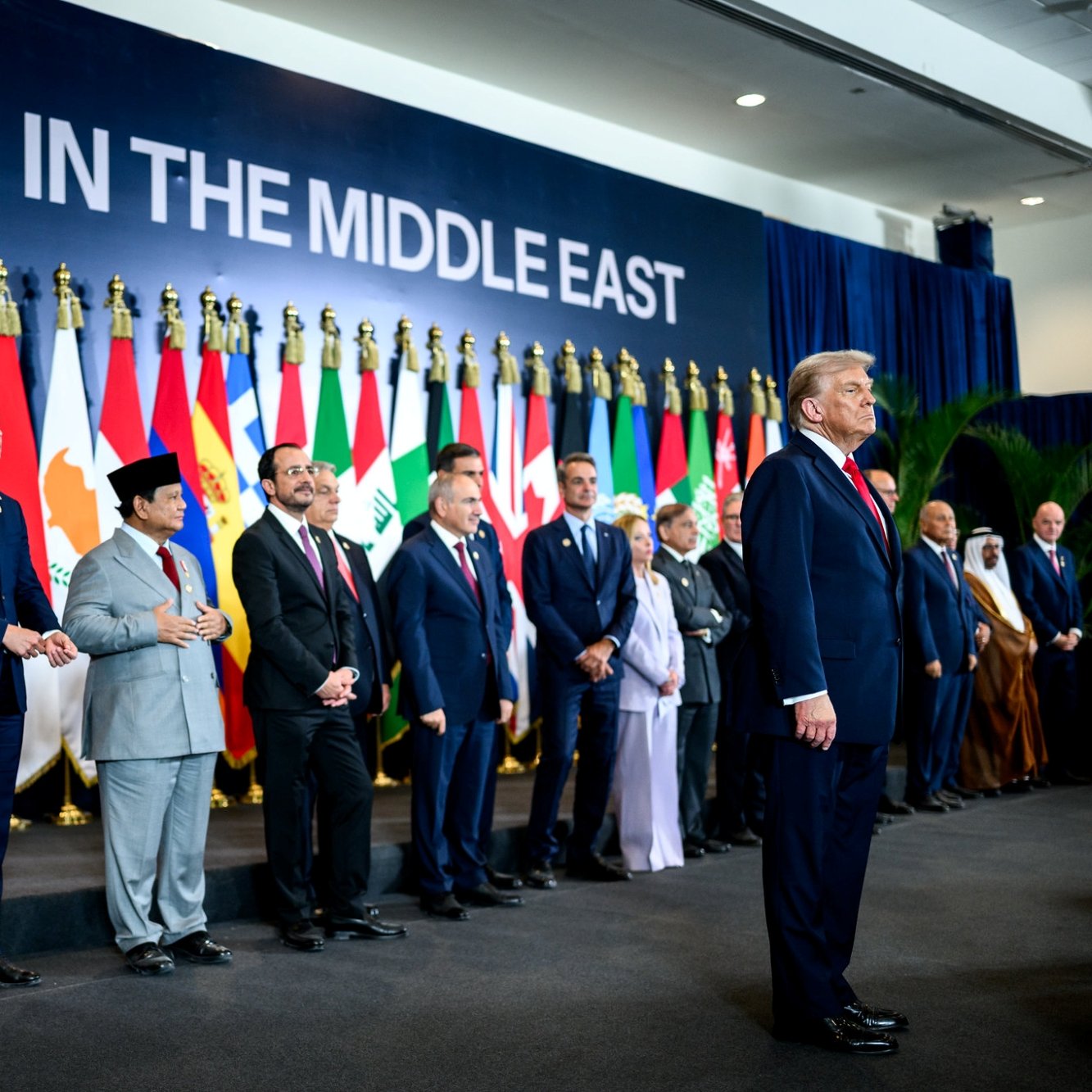 Des dirigeants présents devant un mur avec le texte "PAIX AU MOYEN-ORIENT" et des drapeaux.