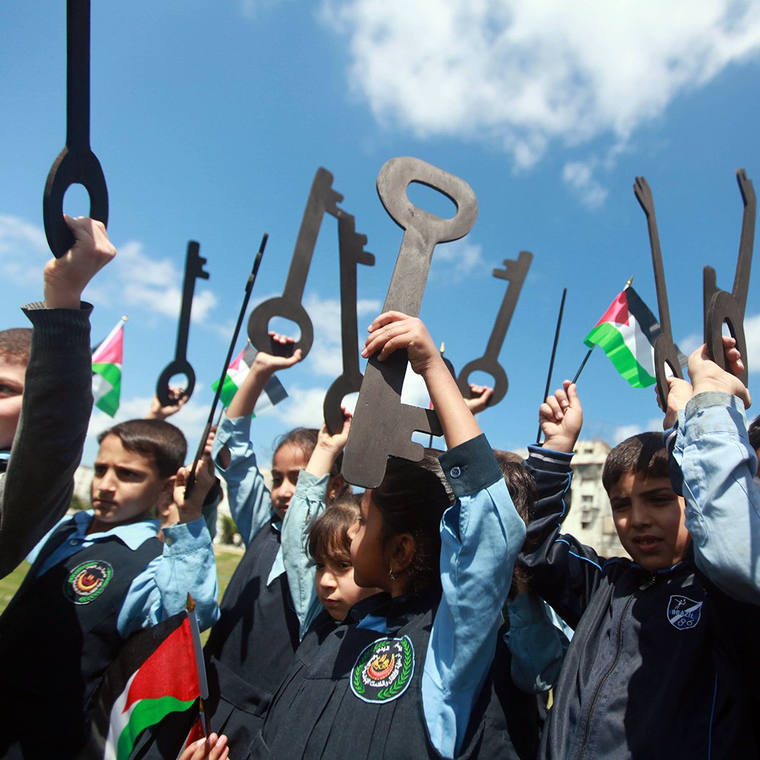 الصورة تظهر مجموعة من الأطفال يقفون في الهواء الطلق، يحملون مفاتيح كبيرة وأعلام فلسطينية. يبدو أنهم يعبرون عن تأييد لقضية معينة أو احتفال بذكرى تاريخية. الأطفال مبتسمون ومتحمسون، مما يعكس روح الفرح والاحتفاء والوعي بالقضايا المتعلقة بفلسطين. السماء صافية وملونة بالغيوم، مما يعطي شعوراً بالحيوية والنشاط.