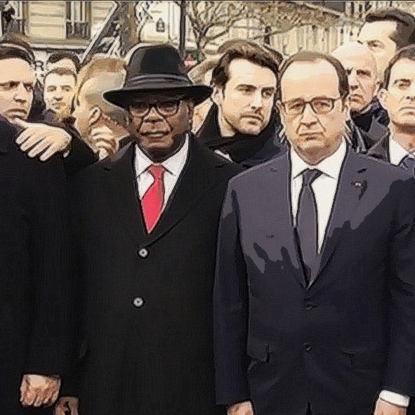 L'image montre un groupe de personnes en émoi, rassemblées dans un cadre public, probablement lors d'un événement solennel. On peut y voir des figures politiques en costumes, dont certaines portent des démarches sérieuses et concentrées. L'ambiance semble être empreinte de gravité et de solidarité. Les participants sont alignés et se regardent, ce qui indique une atmosphère de recueillement ou de soutien mutuel.