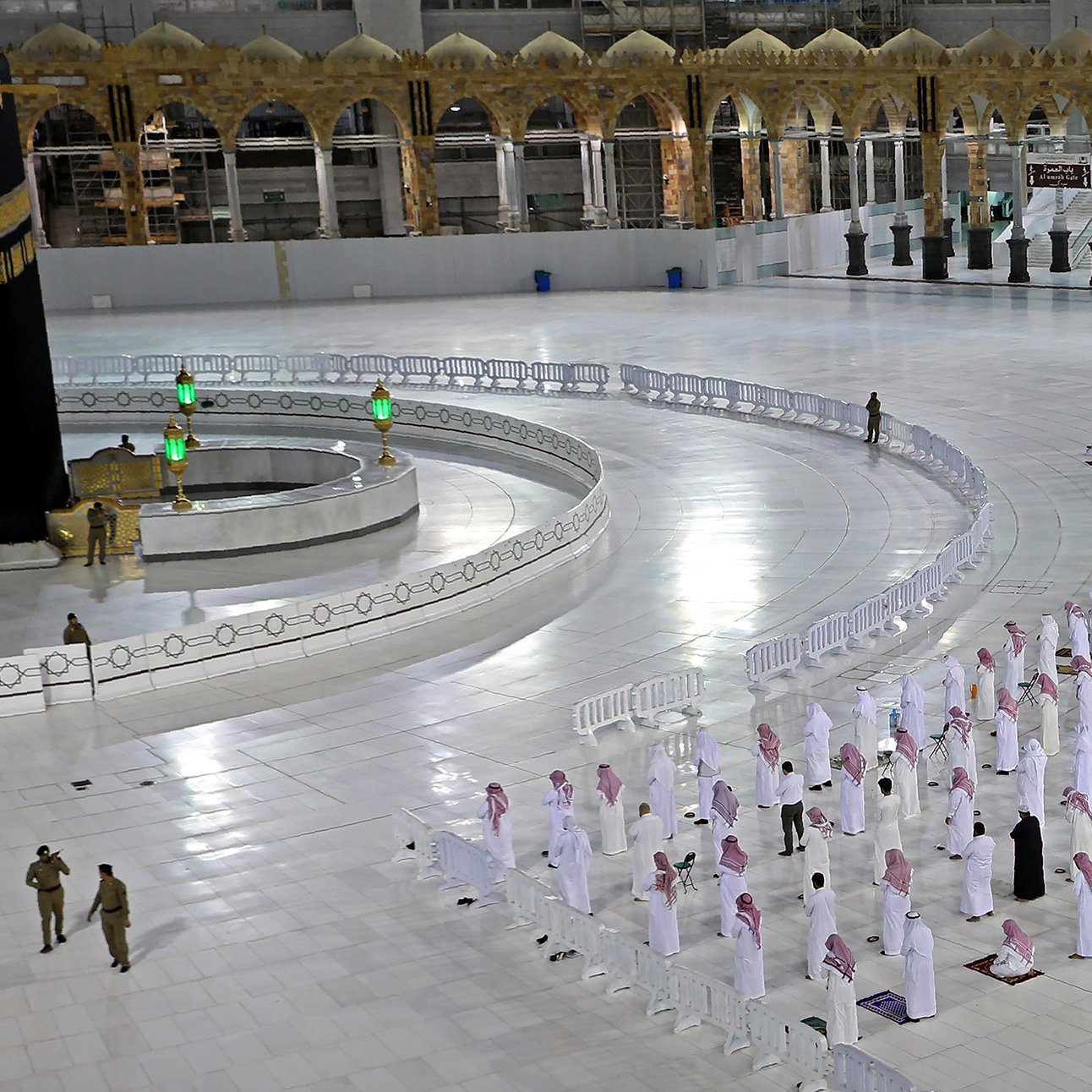 L'image montre une scène à la Kaaba, située à La Mecque. Plusieurs personnes en vêtements traditionnels blancs, souvent appelés " Ihram", sont disposées en rangées, apparemment en train de prier. On peut voir la Kaaba, un cube noir avec des détails dorés, au centre du sanctuaire. Des barrières de sécurité sont présentes pour délimiter les zones, et l'espace est vaste et lumineux, avec des éléments architecturaux en arrière-plan. Cette image évoque un moment de recueillement et de spiritualité dans un lieu sacré pour les musulmans.