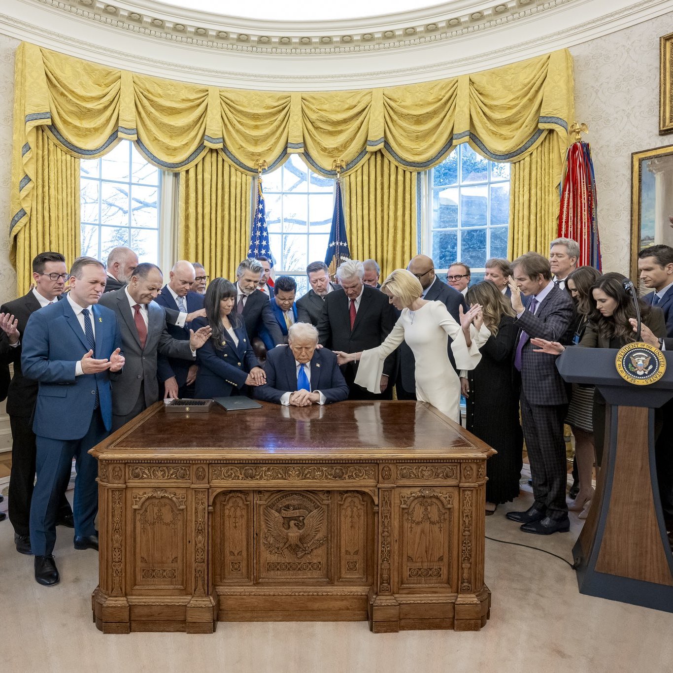 اجتماع رسمي في المكتب البيضاوي مع أشخاص حول طاولة، والدنيا مضاءة خلفهم.