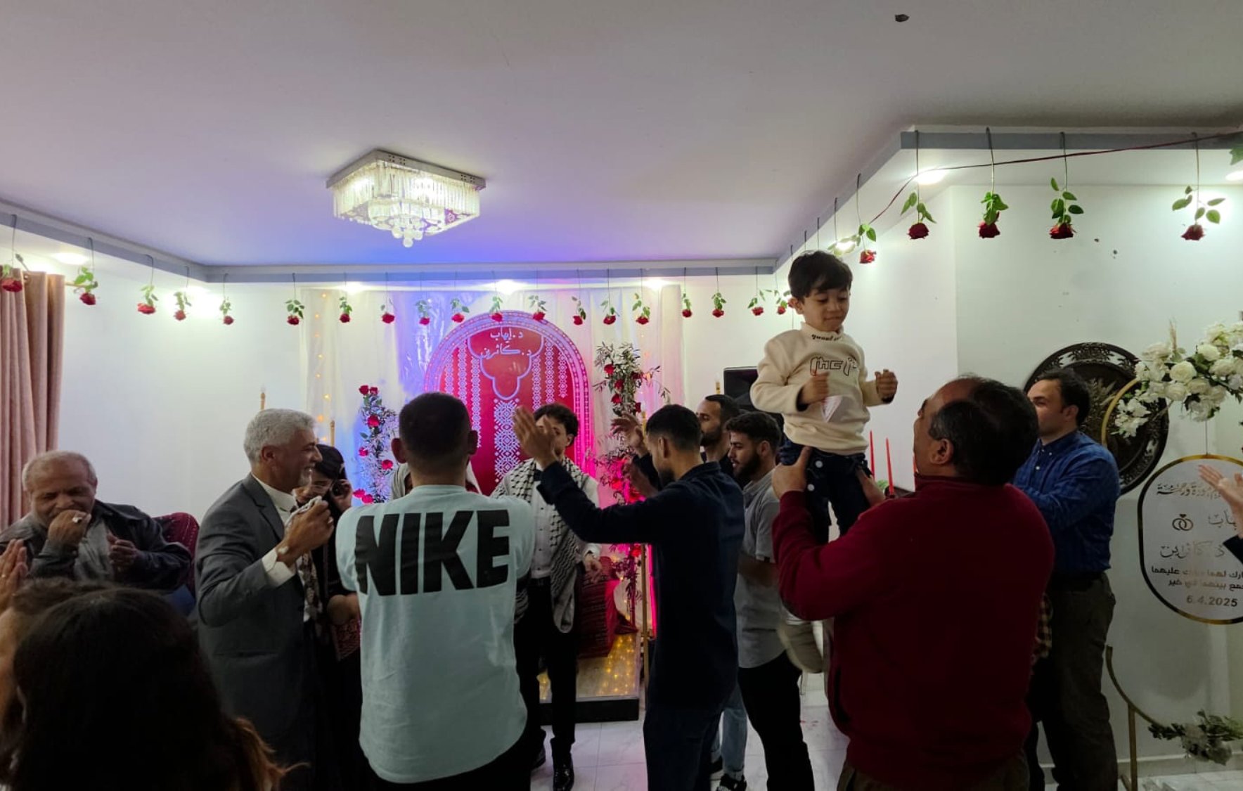 Una festa con persone che ballano, decorazioni floreali e un bambino in braccio.