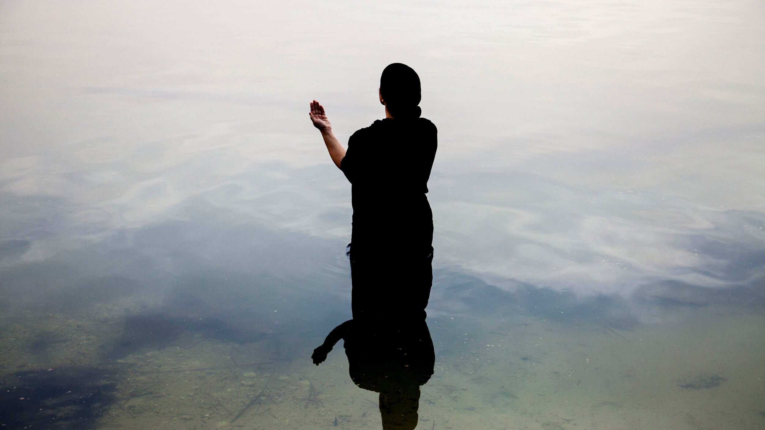 Une silhouette noire se tient dans l'eau calme, reflet visible à la surface.