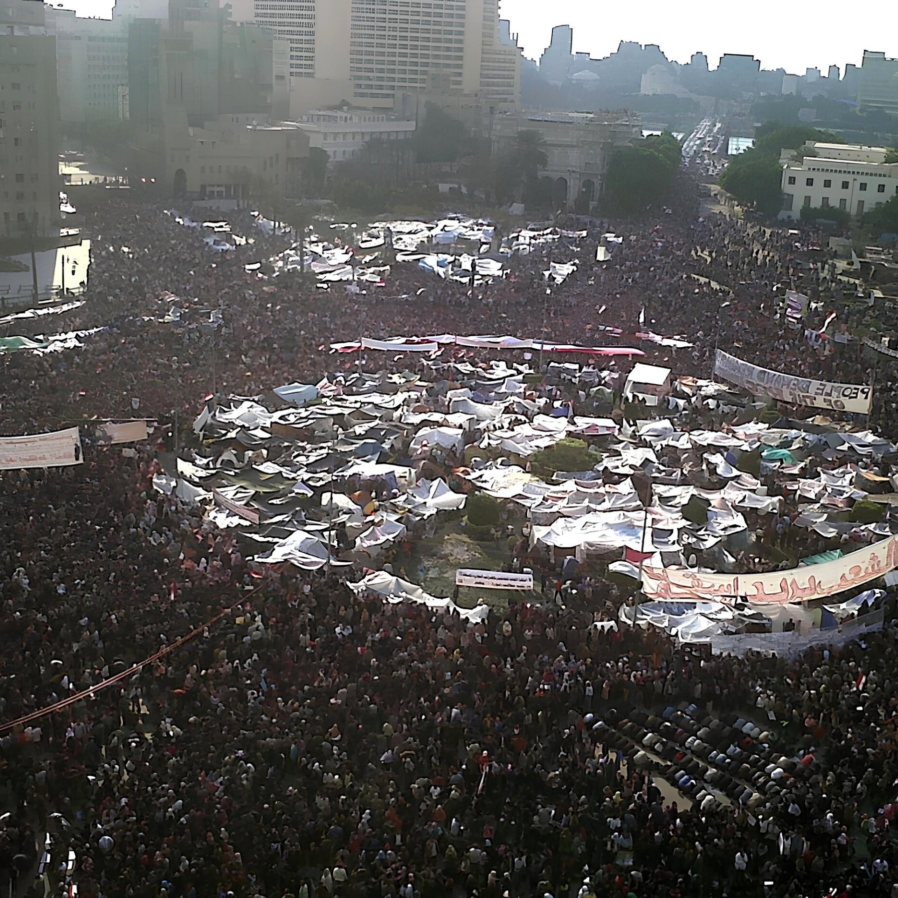 Una grande folla si raduna in una piazza, con tende e striscioni.
