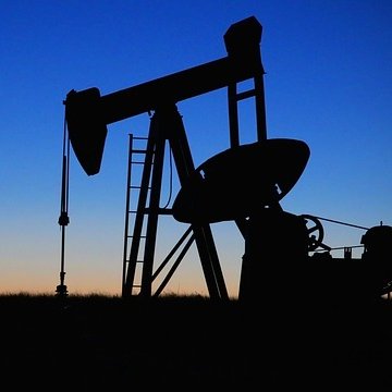 L'image montre un pompage de pétrole silhouetté contre un ciel au crépuscule. On peut voir la structure du pompage avec ses bras articulés, ainsi qu'une échelle menant à la plateforme. Le fond présente des dégradés de bleu et d'orange, indiquant le moment de la journée où le soleil se couche. L'ensemble dégage une ambiance tranquille tout en évoquant l'industrie pétrolière.