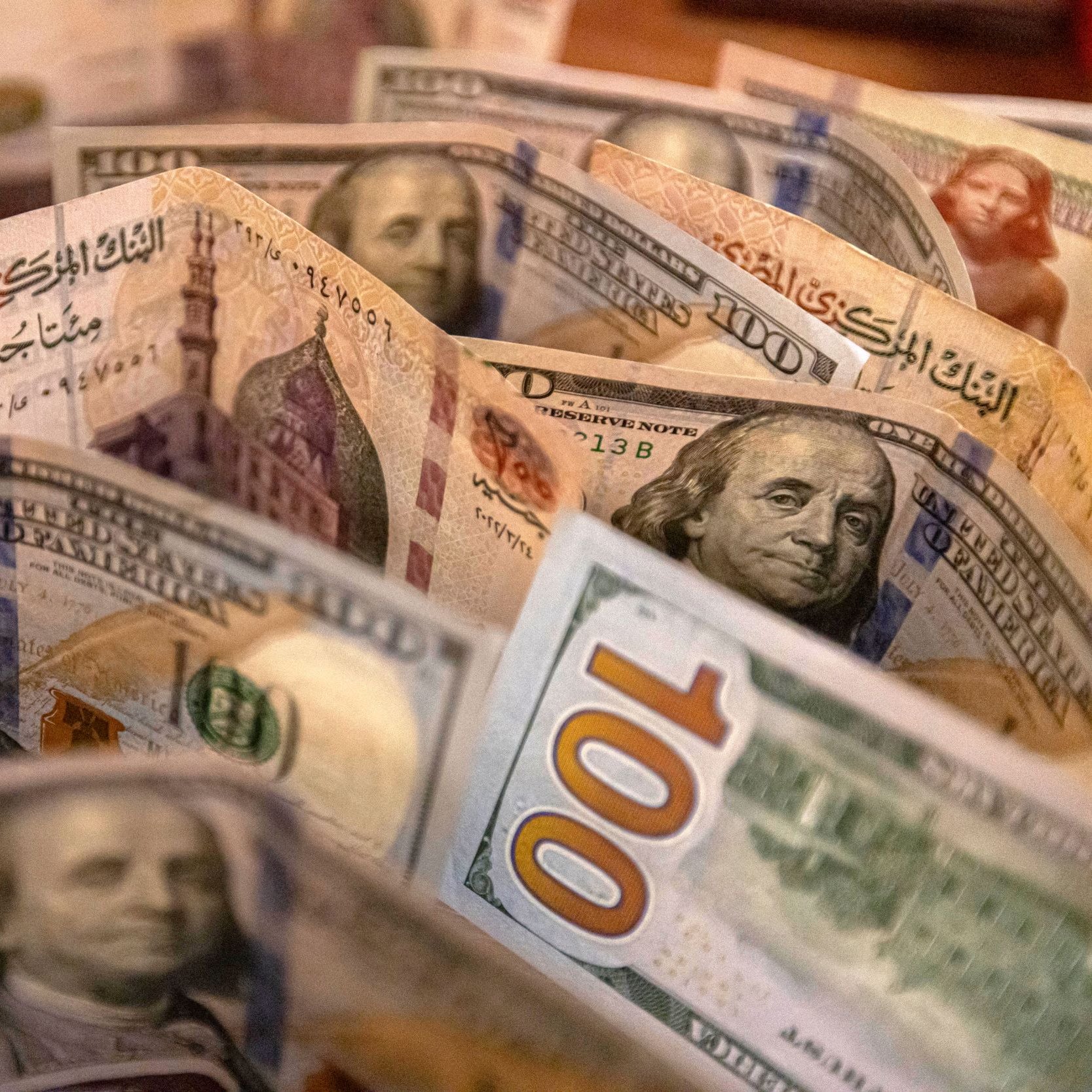 تظهر الصورة مجموعة من الأوراق النقدية الأمريكية من فئة المئة دولار. تتوزع الأوراق بشكل متقارب، مع ظهور وجه بنيامين فرانكلين على الأوراق. الخلفية تشير إلى تفاصيل أخرى، مما يضفي عمقًا للصورة. الألوان بارزة وواضحة، مما يجعل الأوراق النقدية تبدو جديدة وجذابة.