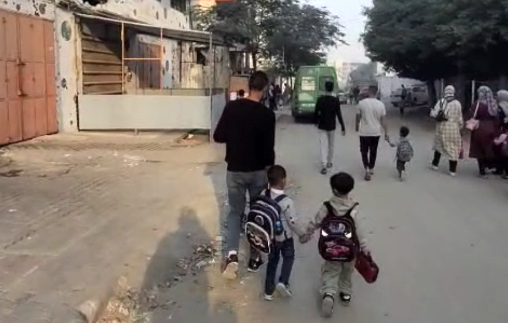 Des enfants marchent main dans la main avec un adulte sur une rue animée.