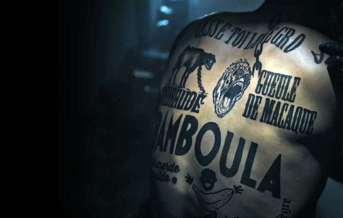 Cette image montre un dos humain couvert de tatouages. Les inscriptions et les illustrations incluent des éléments comme des animaux, des mots en lettres majuscules, et des motifs graphiques. L'éclairage semble sombre, ce qui met en valeur les détails des tatouages. L'ambiance générale est à la fois artistique et intense.